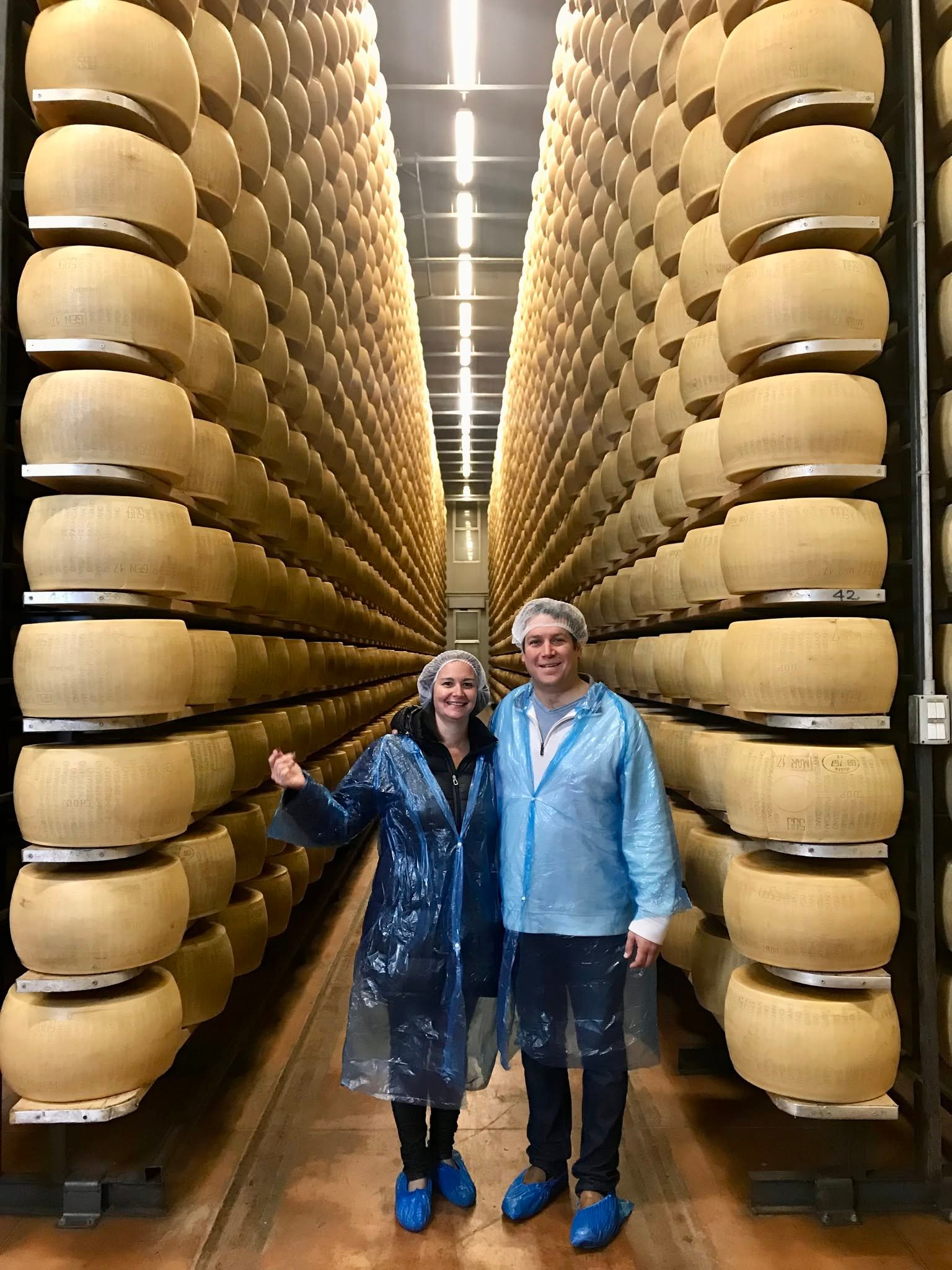 Marcus and Jamie Guiliano standing between rows of Parmigiano Reggiano wheels in an aging room